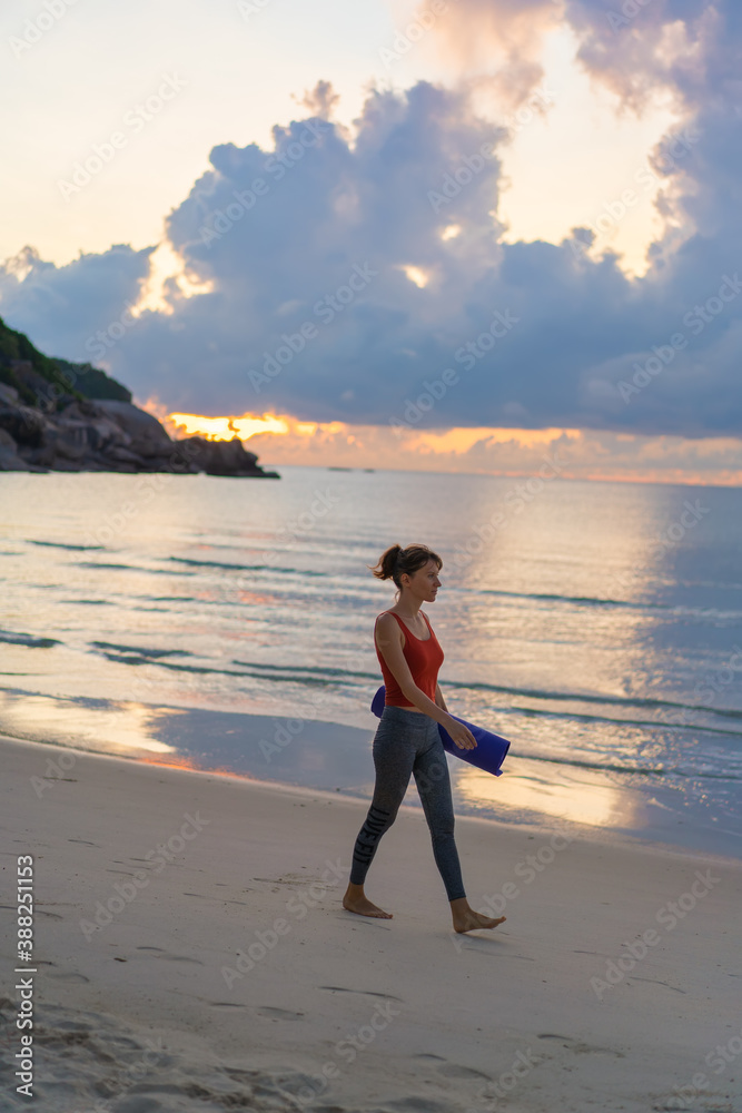 Full length portrait of a smiling sports woman with yoga mat walking