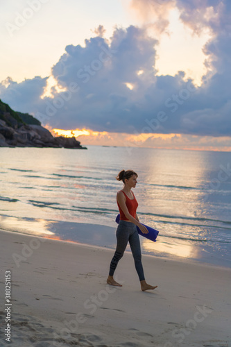 Fototapeta Naklejka Na Ścianę i Meble -  Full length portrait of a smiling sports woman with yoga mat walking