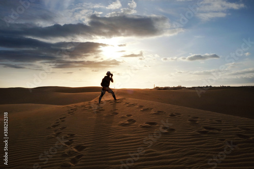 Silhouette of a photographer shooting in the desert of Maspalomas, Gran Canaria at sunset. Sand dunes with footsteps.