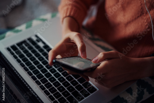 Closeup of young woman hands using smartphone against laptop at home during quarantine