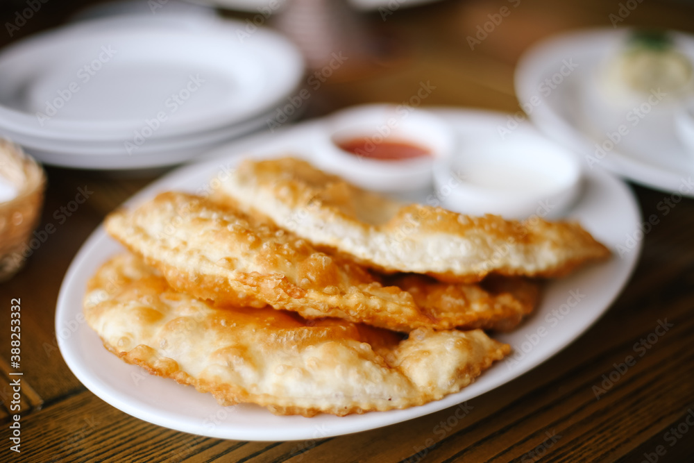 National dish: Chebureks (hot, fragrant, delicious) lie on a white plate with sour cream, ketchup sauces. Crimean cuisine in the restaurant. Closeup. 