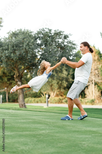 Father and daughter playing in meadow. Father holding daughter and spinning in circles, White and blue colors clothes