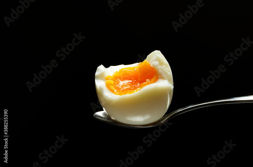 Closeup of half soft boiled egg on the spoon against black background
