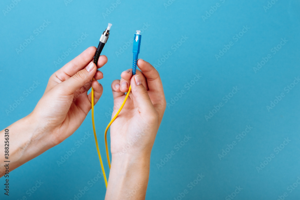 woman's hands hold SC and FC connector fiber optic patch cord single mode on blue background woman's hands hold SC and FC connector fiber optic patch cord single mode on blue background