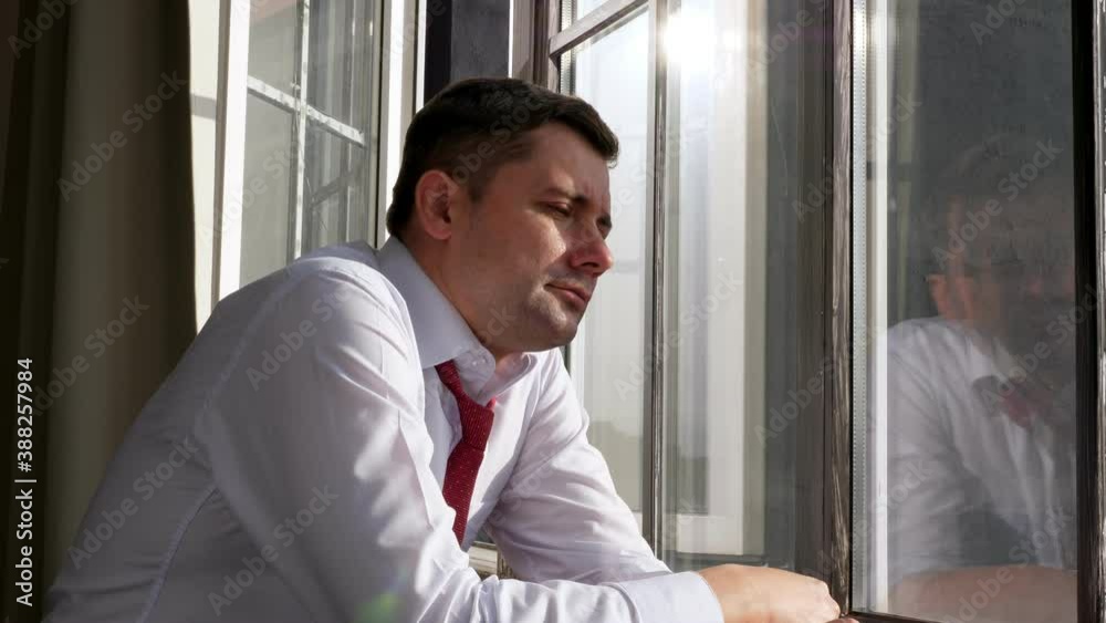 Young businessman at the window looks at the street and has a rest.