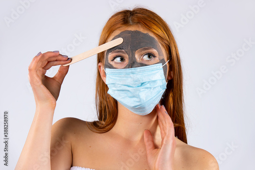 A tired beautiful girl in the salon, with a cosmetic mask on her face and another from a pandemic, shows a stop virus. Beauty, spa, health and covid 19 concept