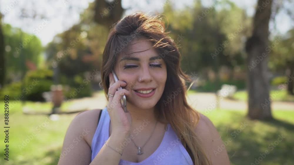 beautiful young latin woman talks on the phone and while she smiles a wind breeze passes over her beautiful young latin woman talks on the phone and while she smiles a wind breeze passes over her
