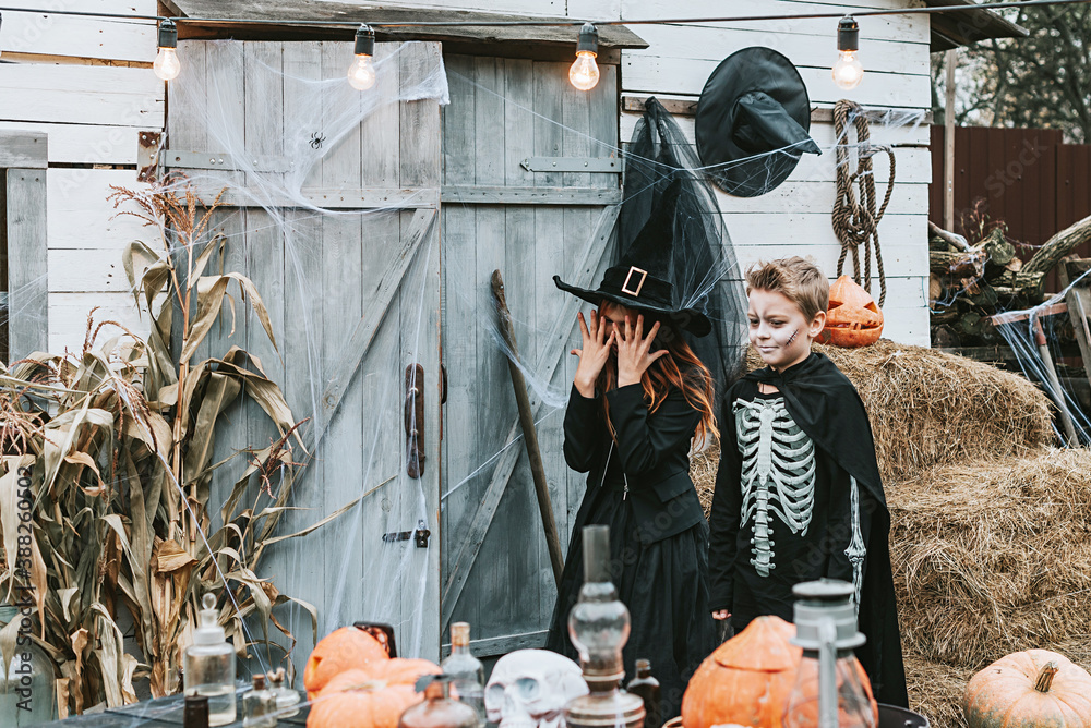 children a boy in a skeleton costume and a girl in a witch costume having fun at a Halloween party on the decorated porch