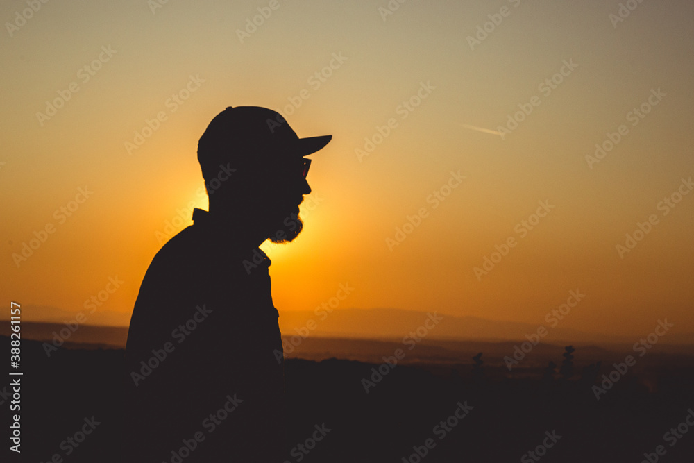 Silhouette of a bearded man with hat up on the hill in the sunset