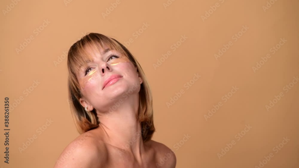 Beautiful smiling woman with short hair in gold eye patches looking in camera and smiling over colorful gold background. Beauty concept Beautiful smiling woman with short hair in gold eye patches looking in camera and smiling over colorful gold background. Beauty concept