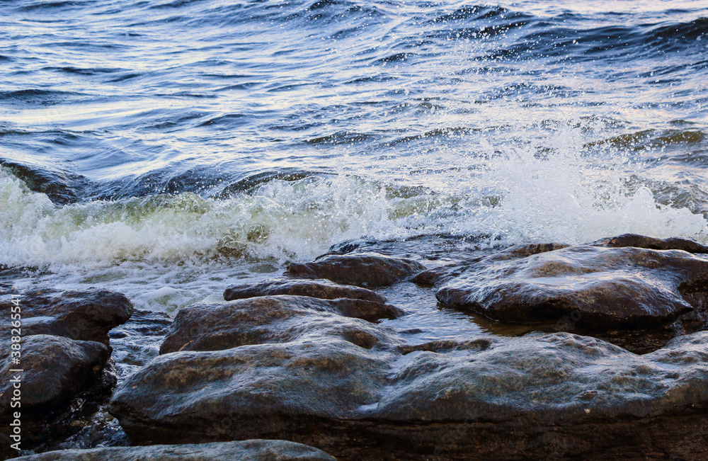 waves run onto the shore and crash against the rocks, creating many splashes and splashes near the shore. river surf in stormy weather near a stone pebble coast with foamy splashing waves. waves run onto the shore and crash against the rocks, creating many splashes and splashes near the shore. river surf in stormy weather near a stone pebble coast with foamy splashing waves.