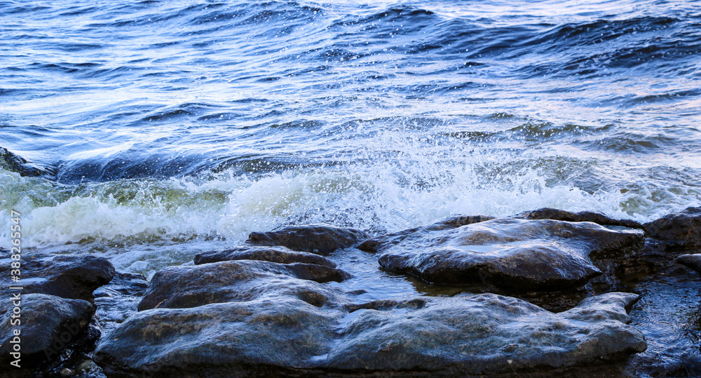 waves run onto the shore and crash against the rocks, creating many splashes and splashes near the shore. river surf in stormy weather near a stone pebble coast with foamy splashing waves. waves run onto the shore and crash against the rocks, creating many splashes and splashes near the shore. river surf in stormy weather near a stone pebble coast with foamy splashing waves.