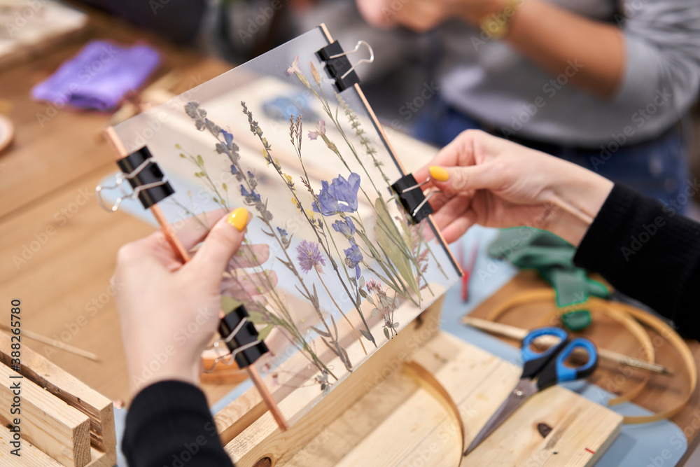 A woman fixes glass plates.. Master class on creating frame with Herbarium in tiffany technique in stained glass. Herbarium of dried different plants and flowers placed under a glass A woman fixes glass plates.. Master class on creating frame with Herbarium in tiffany technique in stained glass. Herbarium of dried different plants and flowers placed under a glass