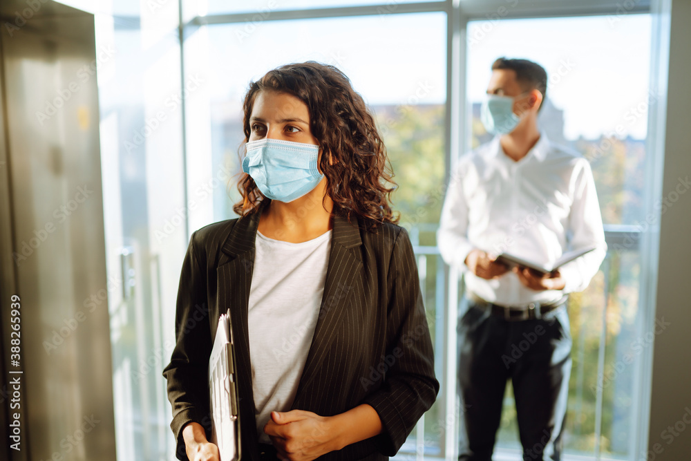 Portrait of businesswoman in protective face mask during virus epidemic while standing near elevator at modern office. Office manager back at work in office after quarantine. Covid-19.