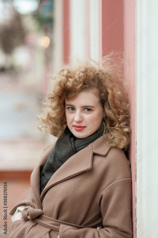 Portrait of a young woman with curly hair outdoors. Girl standing leaning against the wall Portrait of a young woman with curly hair outdoors. Girl standing leaning against the wall