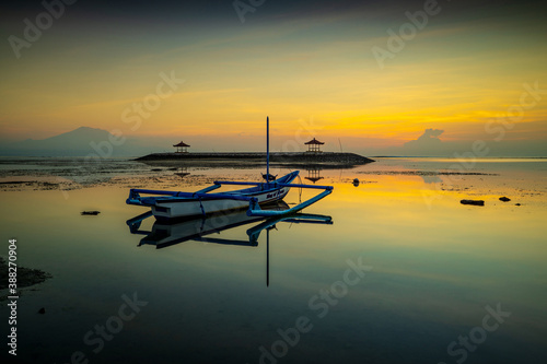 Seascape. Traditional fisherman boat jukung. Sunrise landscape. Gazebos on an artificial island in the ocean.  Water reflection. Slow shutter speed. Soft focus. Sanur beach, Bali.