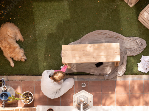 BLOND WOMAN IN PAJAMA, HOUSEWIFE, GIVING WAX TO WOODEN BENCH WITH PINK RUBBER GLOVES