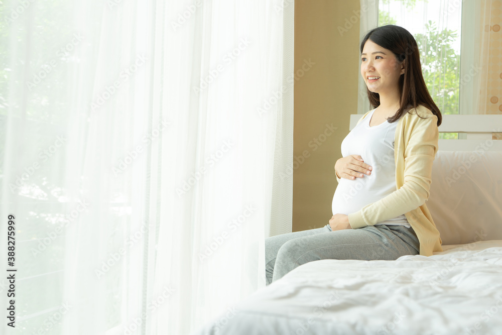 Happy smiling pregnant woman touching belly sitting in bed at home. Happy smiling pregnant woman touching belly sitting in bed at home.