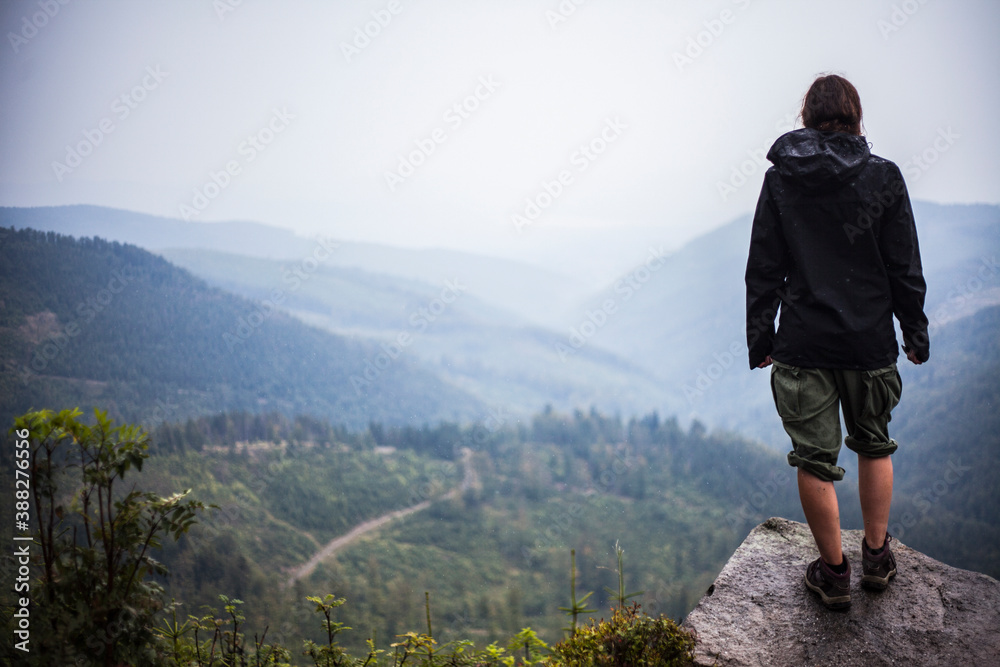 A person standing on a stone in the mountains overlooking the valley.