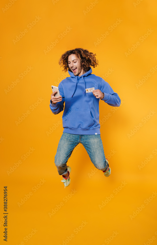 Excited caucasian guy jumping with cellphone and credit card Excited caucasian guy jumping with cellphone and credit card