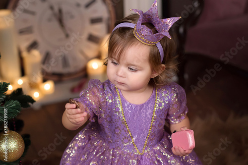 Little princess in elegant ball gown and diadem holding jewelry in hands