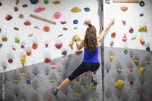 young fit woman climber moving up on rock wall, climbing on artificial wall indoors.