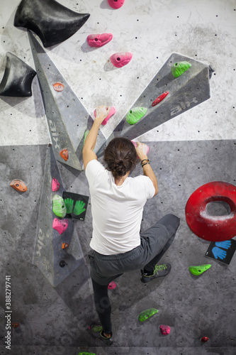 young fit male climber moving up on rock wall, climbing on artificial wall indoors.