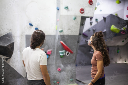 young fit woman and man climbers wearing mask on steep rock wall indoors