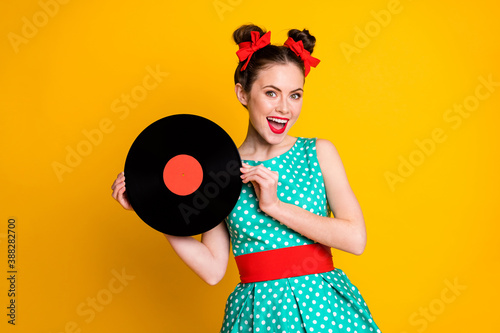 Portrait of lovely cheerful girl holding in hands vinyl disc having fun isolated on vibrant yellow color background