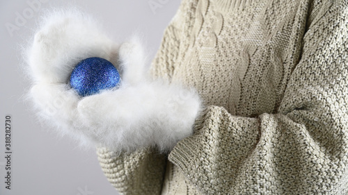 Female hands in warm mittens hold a Christmas blue ball . Winter holidays sales.