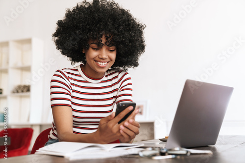 Smiling african american girl using cellphone while studying with laptop