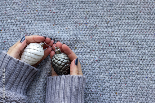 Female hands in knitted sweater with Christmas tree pine cones and with beautiful manicure - dark gray blue glittered nails on knitted background with copy space