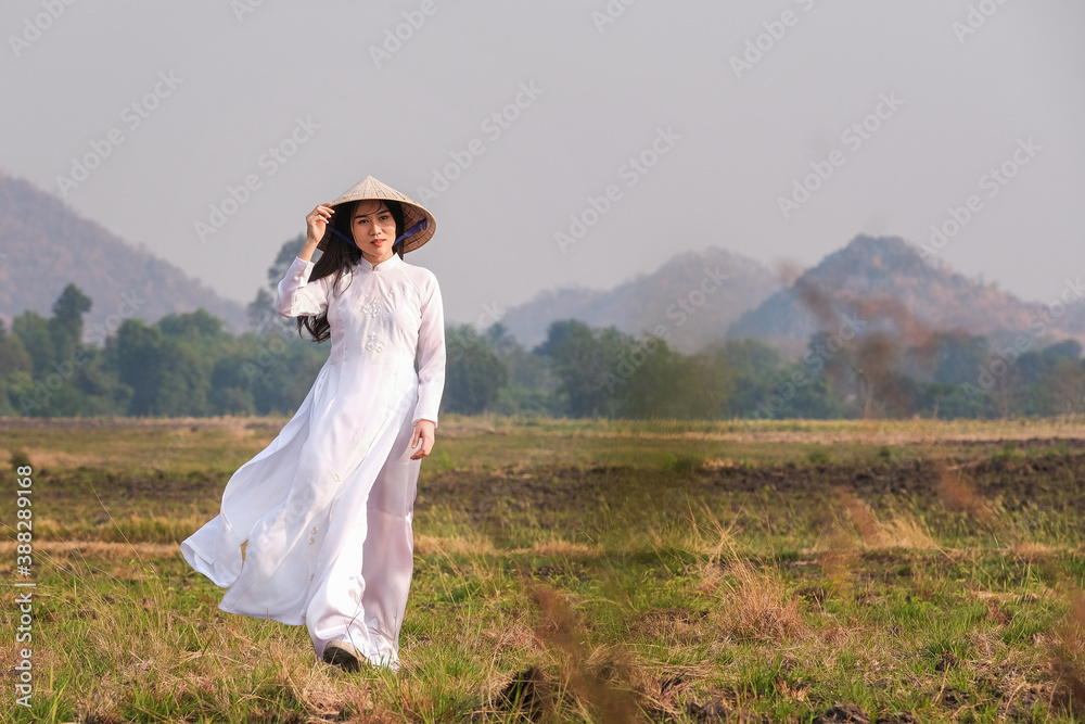 Vietnamese girl in white dress wearing a hat walks in the field