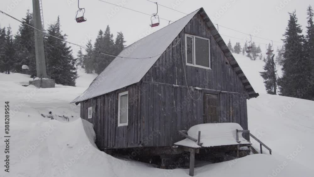 Old wooden house under a chair lift in the mountains on a ski resort in a snow fall Old wooden house under a chair lift in the mountains on a ski resort in a snow fall