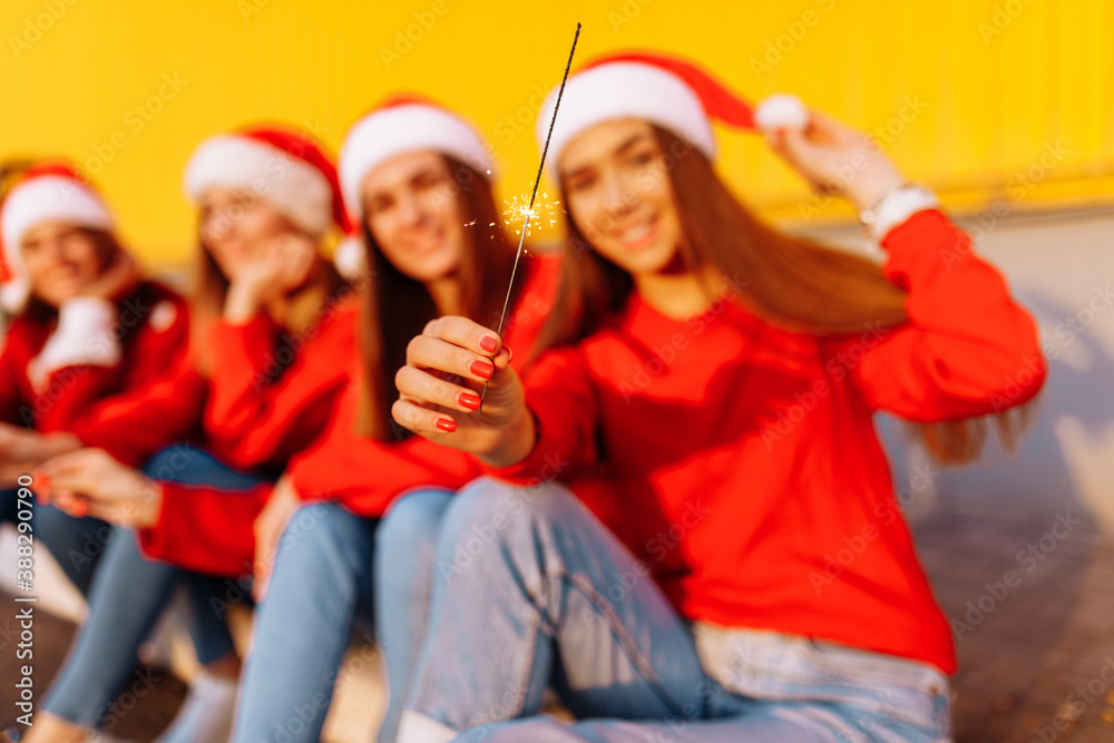 Obraz premium Company of cheerful young women celebrating the New Year in Santa Claus hats, with sparklers