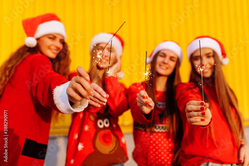 Happy young women in santa claus hats with christmas sparklers having fun and celebrating new year
