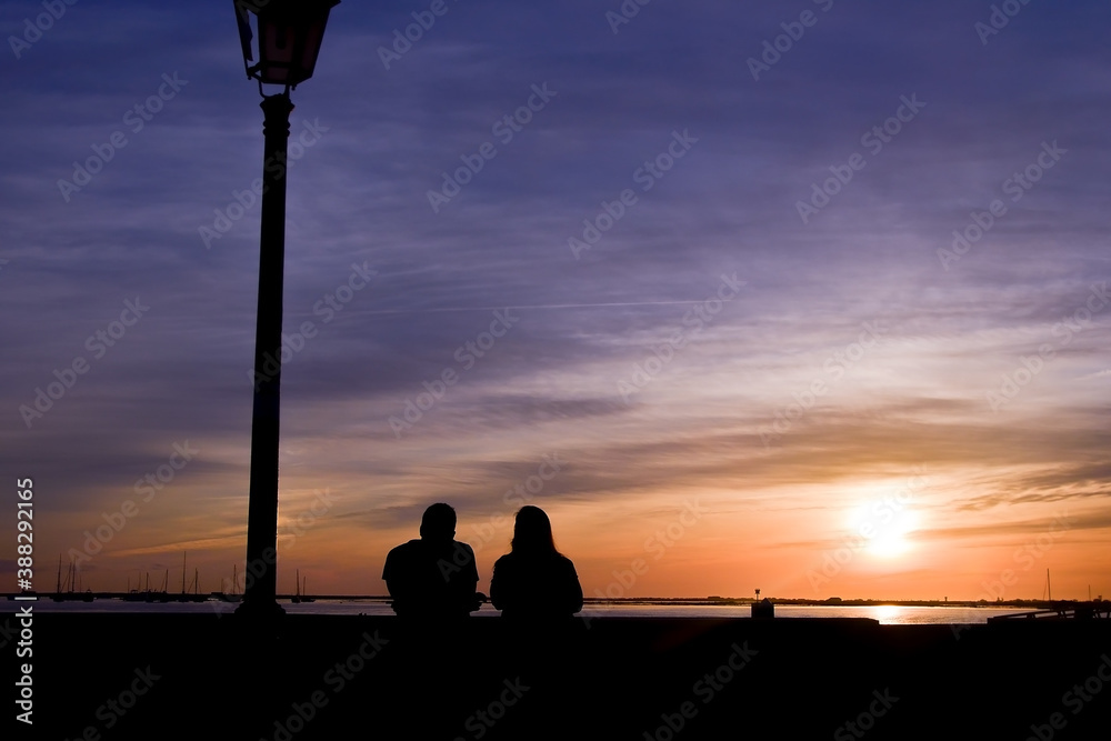 Silhouette of a couple in love on the waterfront in the city of Faro. colorful sunset on the beach..