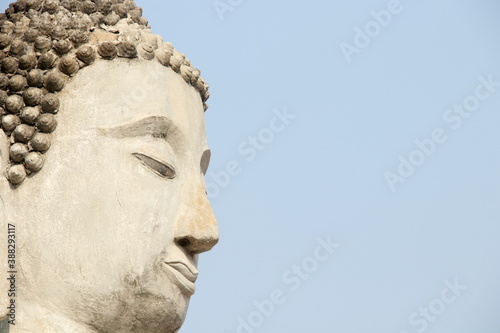Face of ancient cement Buddha statue and light blue sky background in Ayutthaya province, Thailand. Beside view.