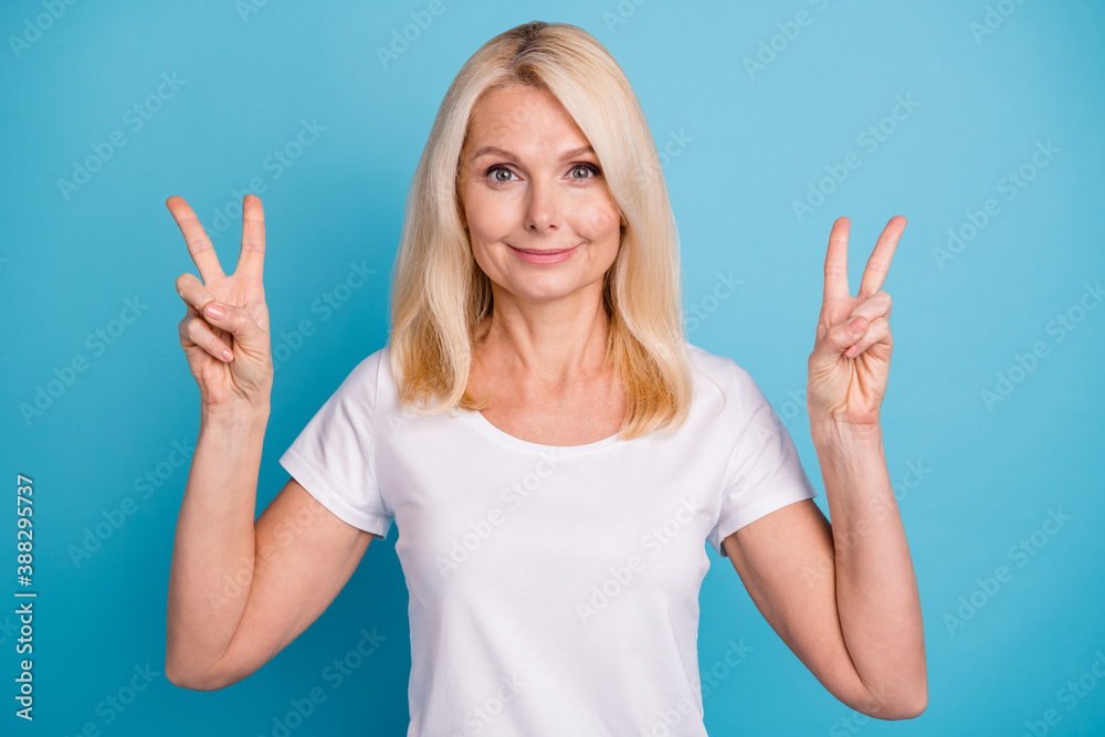Photo of attractive aged lady showing both hands arms v-sign symbols wear casual white t-shirt isolated blue color background Photo of attractive aged lady showing both hands arms v-sign symbols wear casual white t-shirt isolated blue color background