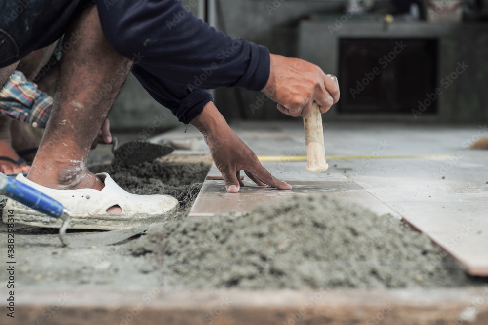 Motion blurred hand of worker installing the floor tile by wooden hammer at the construction site Motion blurred hand of worker installing the floor tile by wooden hammer at the construction site