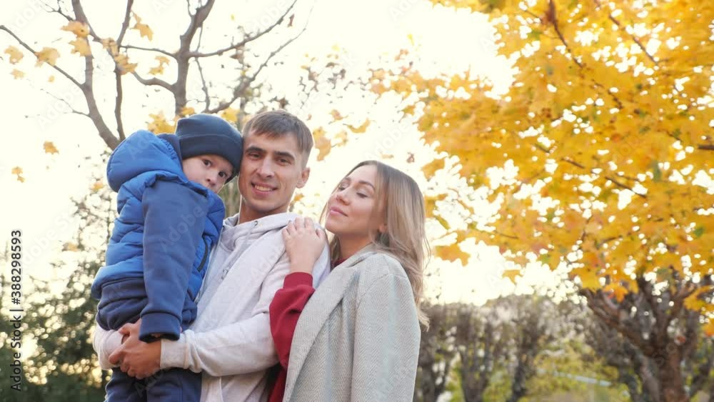 Lovely family of mother father and funny little boy hug looking at camera in picturesque autumn city park on nice warm day. Lovely family of mother father and funny little boy hug looking at camera in picturesque autumn city park on nice warm day.