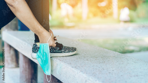 Fitness woman take off her surgical mask getting ready to do run exercise lacing running shoes for outdoor jogging. New normal lifestyle. Health care concept. Selective focus on surgical mask.