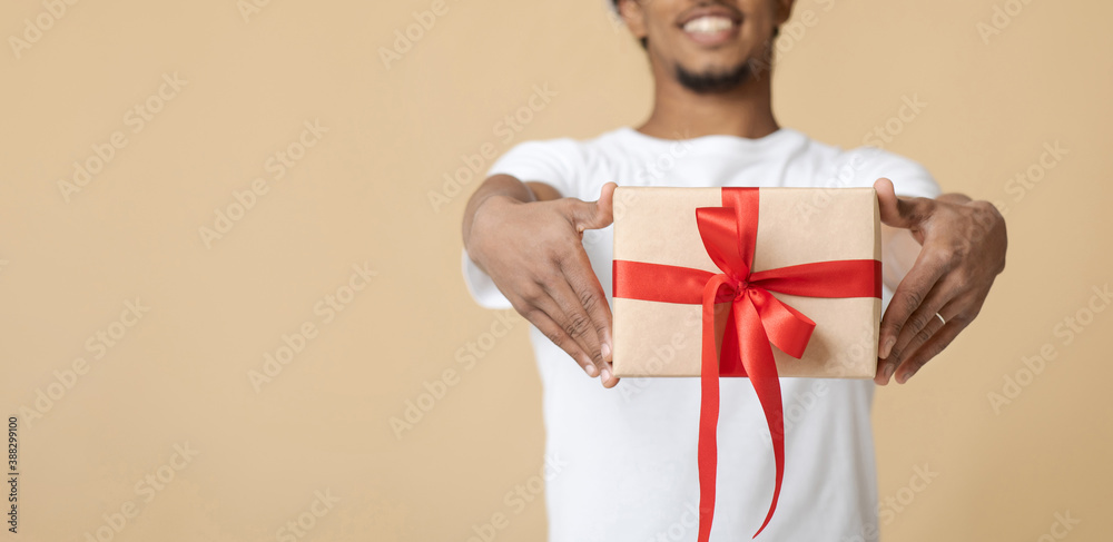 Smiling young african american man in white t-shirt giving gift box with present with red ribbon Smiling young african american man in white t-shirt giving gift box with present with red ribbon
