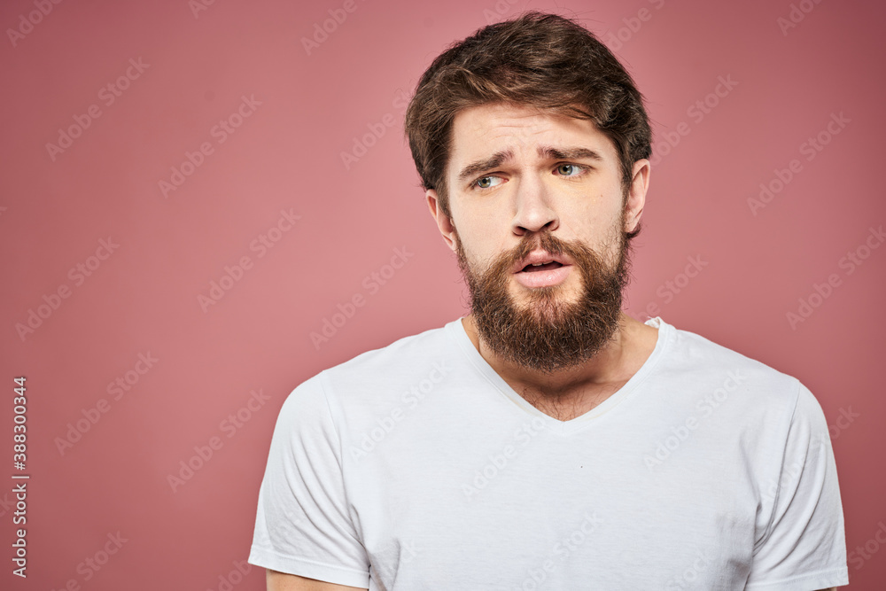 Fototapeta premium Emotional bearded man in white T-shirt discontent pink background