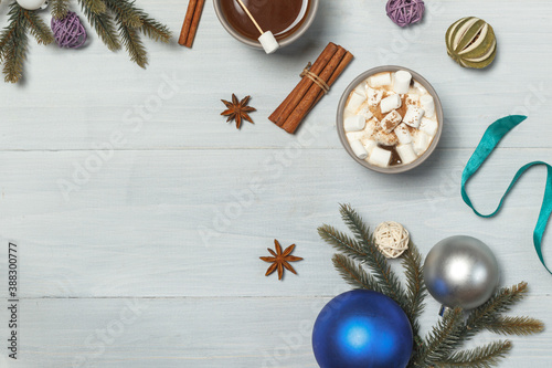 Hot cocoa with melting marshmallows on a light wooden background, with spruce branches and decorations. New Year's background with space, horizontally