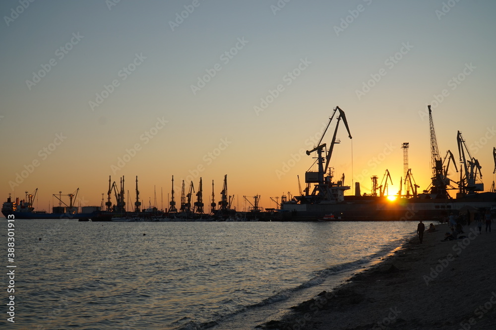 Silhouettes of cranes and ships against the setting sun.