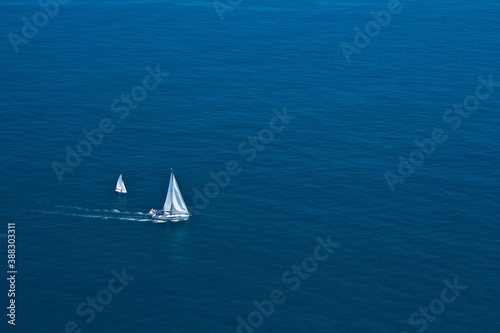 Aerial view on two white sailboats leaving wake in the blue Mediterranean sea .