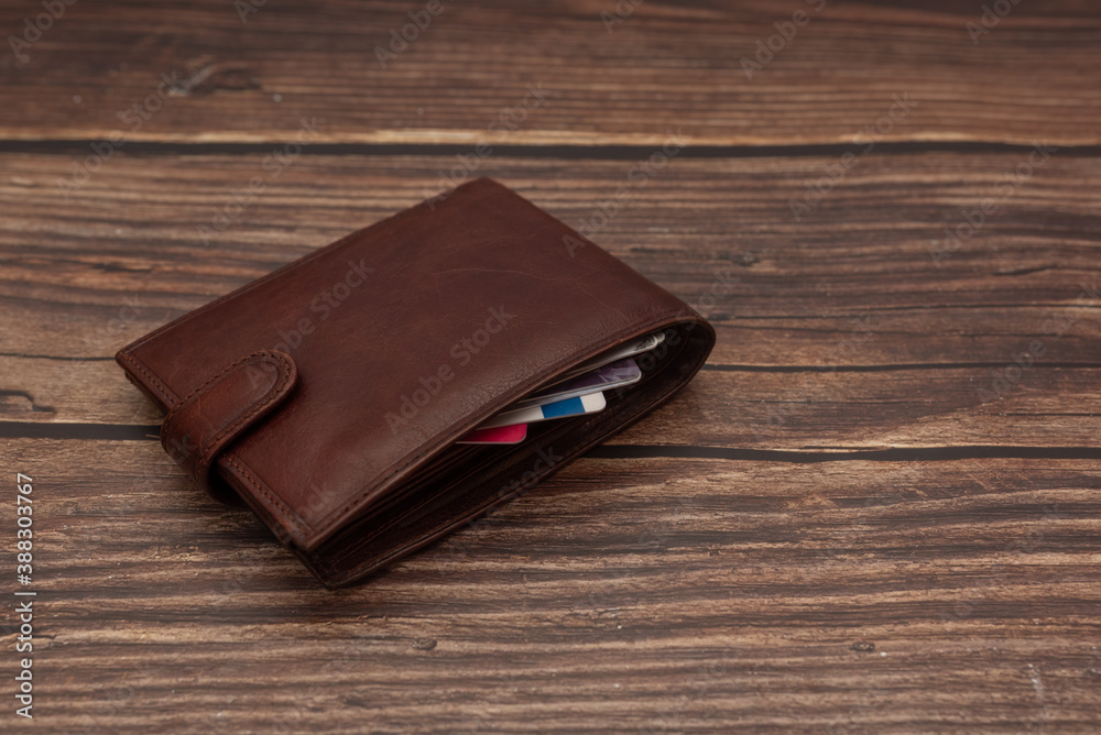 Closed men's brown wallet on a wooden brown background with business cards Closed men's brown wallet on a wooden brown background with business cards