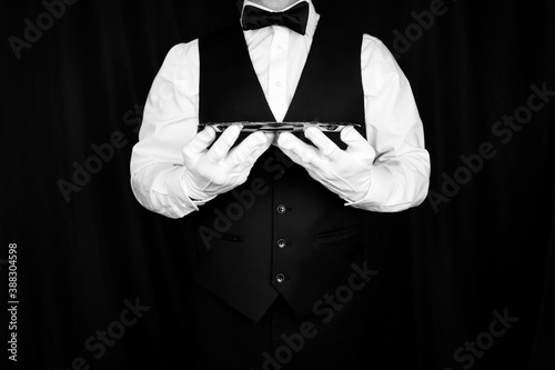 Portrait of Butler or Waiter in Black Vest and Bow Tie Holding Silver Tray. Concept of Service Industry and Professional Hospitality. Dependable Servant. Copy Space for Service. White Glove Service