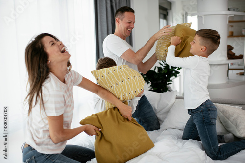 Young parents with sons fighting pillows on the bed. Happy mother and father with boys having fun at home.. photo